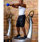 Man using silver Power Plate vibration trainer while holding blue kettlebell, wearing white tank top and black shorts against