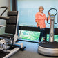 Woman in coral shirt demonstrating silver and black Power Plate Pro5 vibration plate trainer in office gym setting