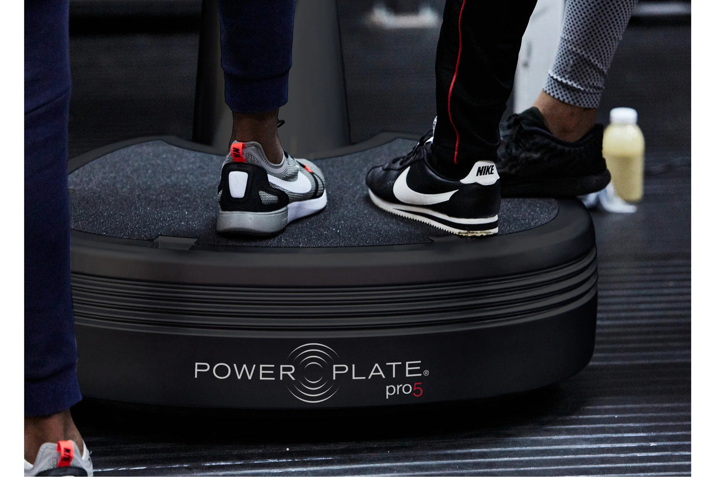 Multiple people wearing athletic sneakers standing on black Power Plate Pro5 vibration training platform