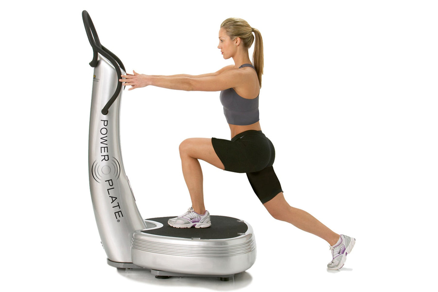 Woman using silver and black Power Plate vibration trainer with black handles, performing lunge exercise on white background