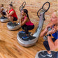 Multiple people using silver and black Power Plate vibration training machines in a fitness studio with brick walls