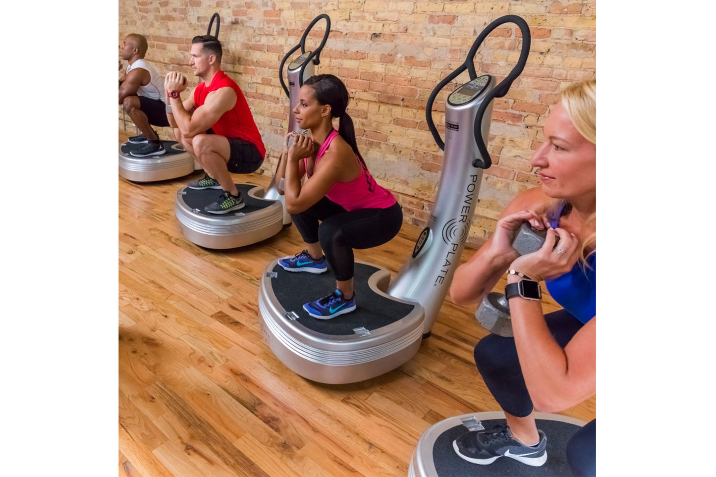 Multiple people using silver and black Power Plate vibration training machines in a fitness studio with brick walls