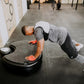 Man in white cap and gray shirt performing plank exercise on black Power Plate vibration trainer in gym setting