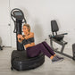 Woman using black Power Plate Pro8 vibration plate trainer in gym setting with exercise equipment