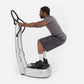 Man using white and black Power Plate vibration trainer with dual handles, wearing gray shirt and dark shorts