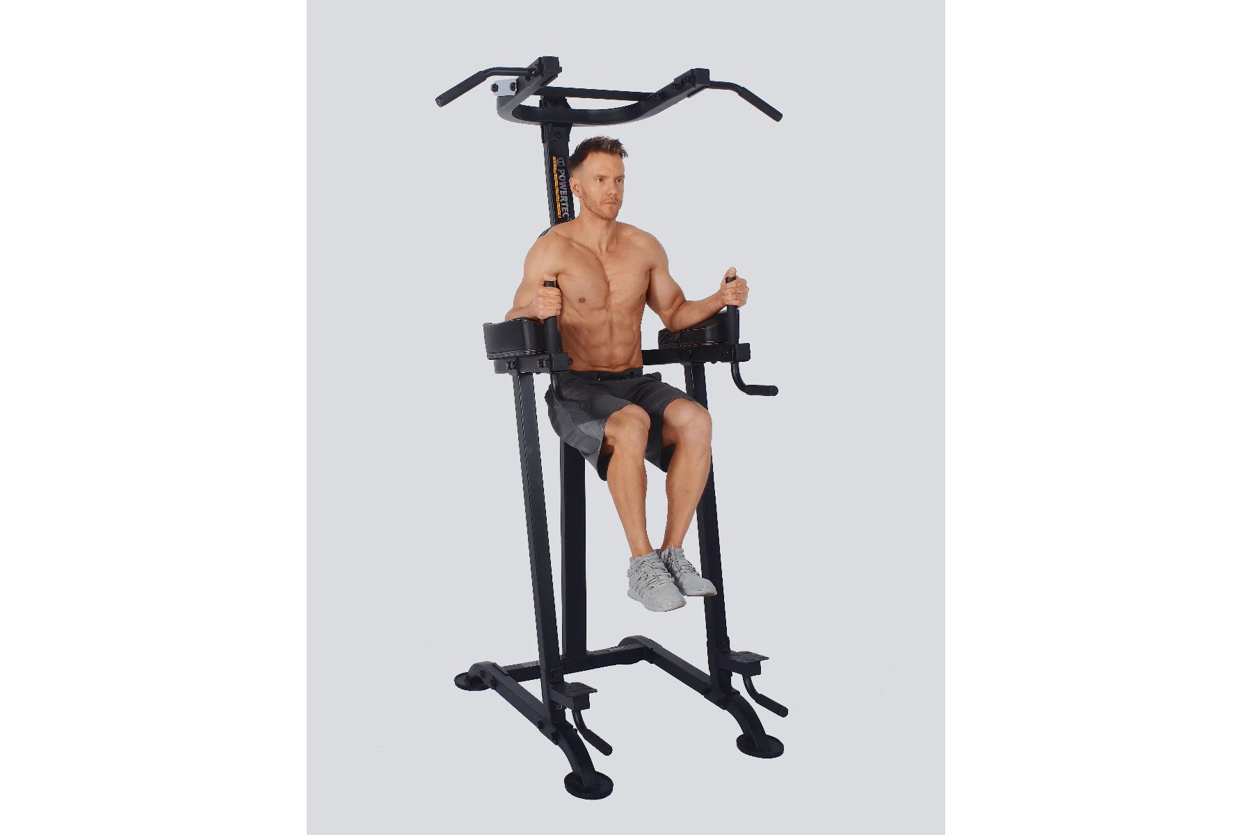 Black multi-function power tower with pull-up bar and leg raise station, demonstrated by shirtless male model on gray backgro