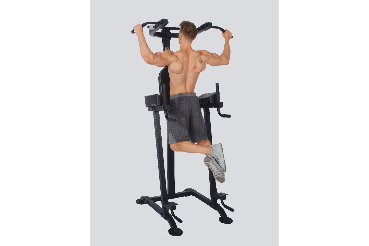 Black vertical power tower with pull-up bar, dip station, and leg raise attachment, demonstrated by shirtless male model on g