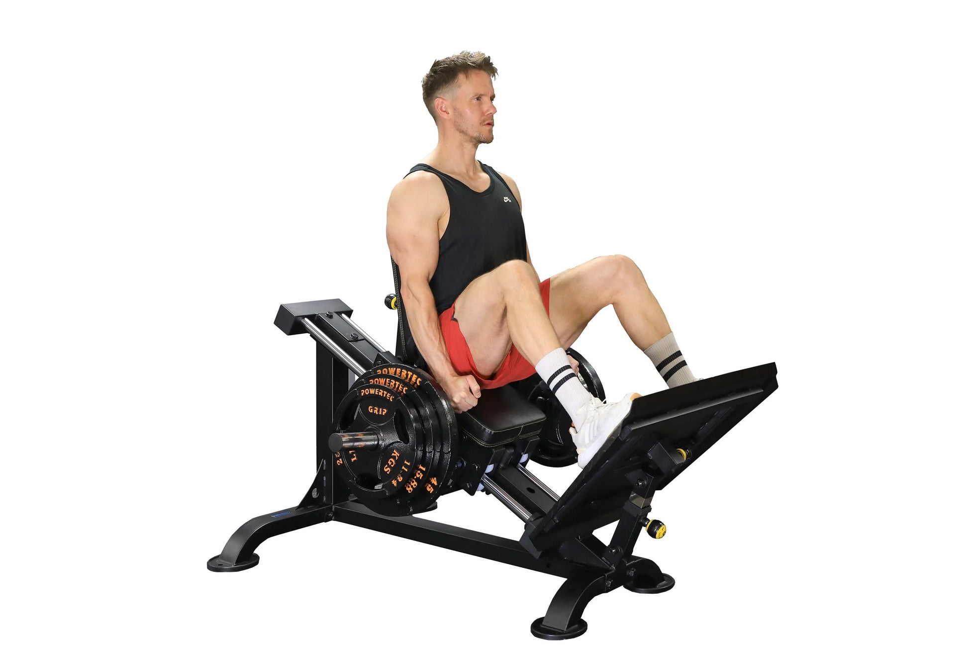 Man using black Powertec Leg Sled machine with weight plates, wearing black tank top and red shorts, on white background
