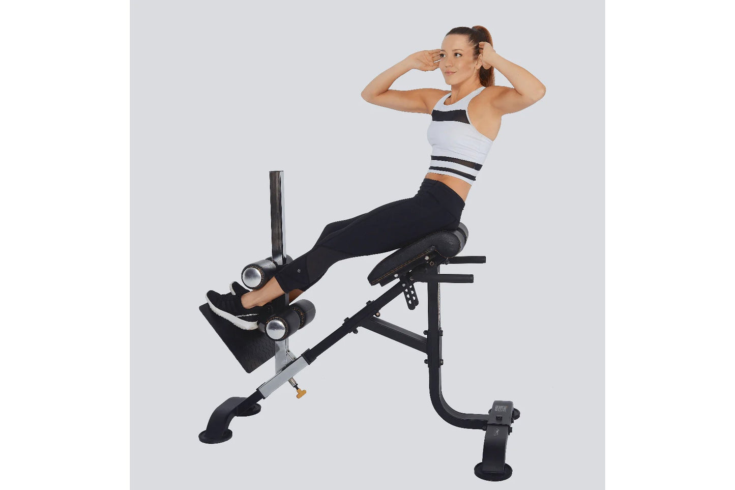 Woman wearing white and navy sports bra and black leggings using black Powertec dual hyperextension/crunch machine on gray ba