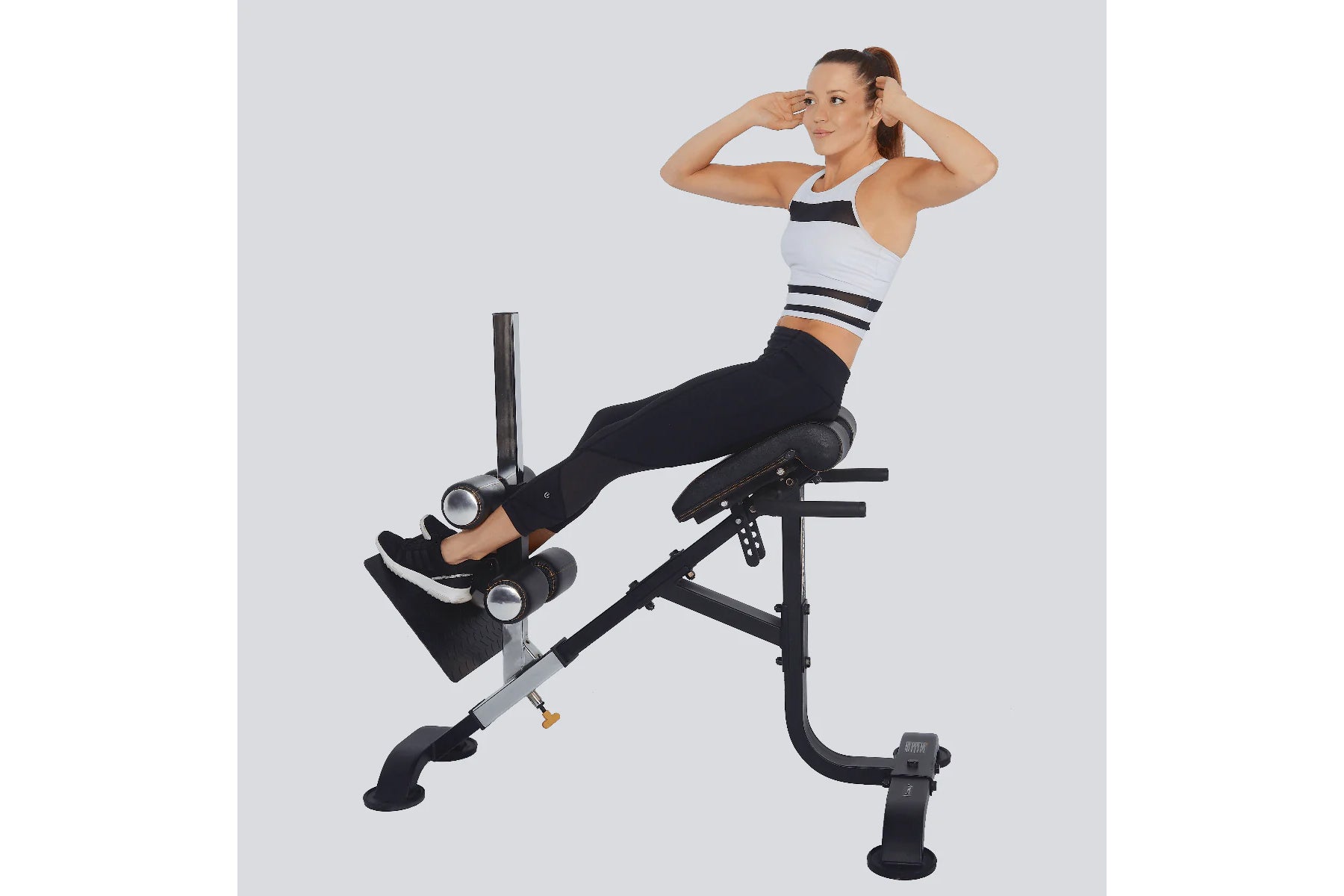 Woman wearing white and navy sports bra and black leggings using black Powertec dual hyperextension/crunch machine on gray ba