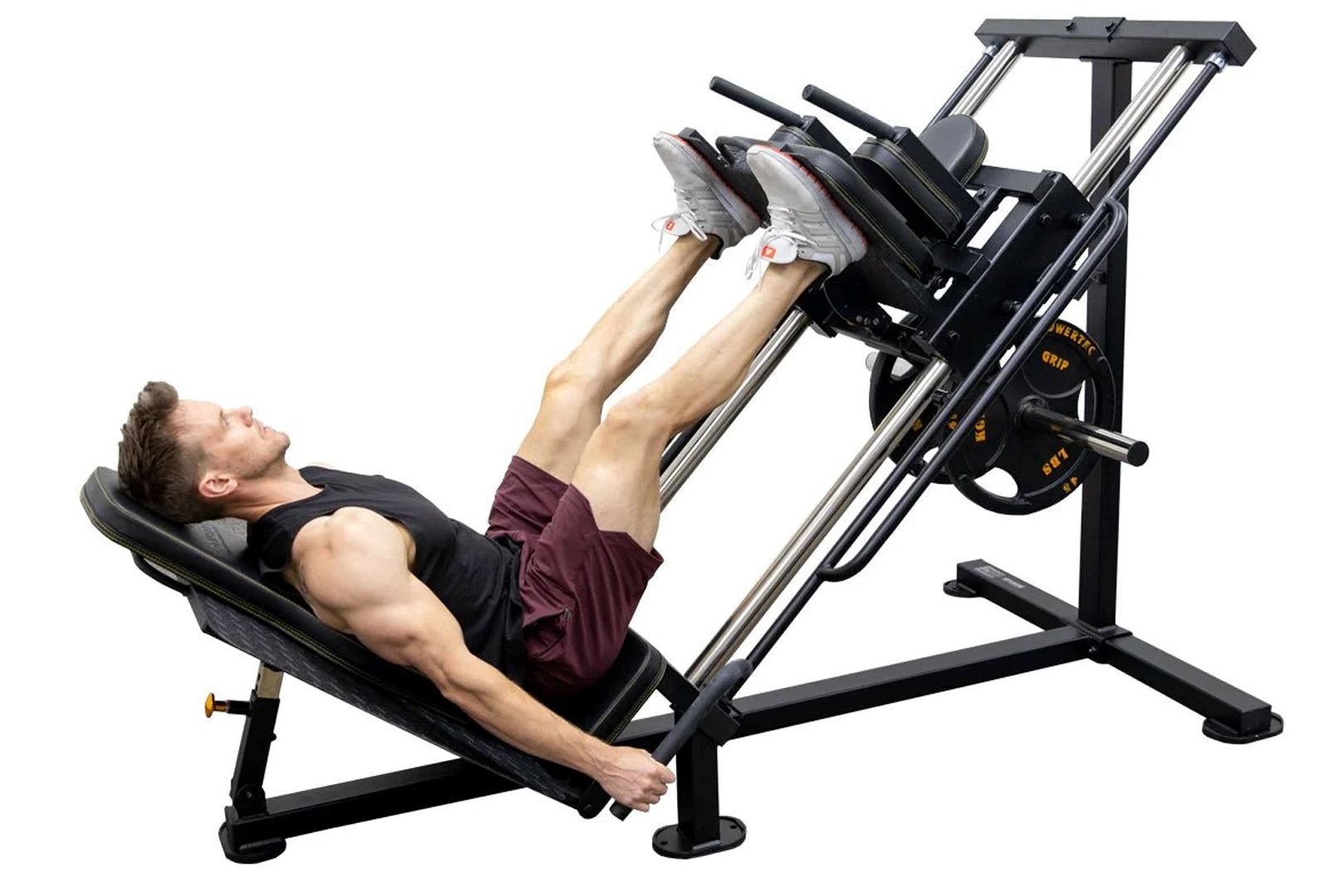 Man using black and silver leg press machine with weight plates, demonstrating seated leg exercise position on white backgrou