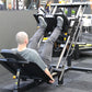 Person using black and silver leg press hack squat combo machine in gym setting, demonstrating exercise form