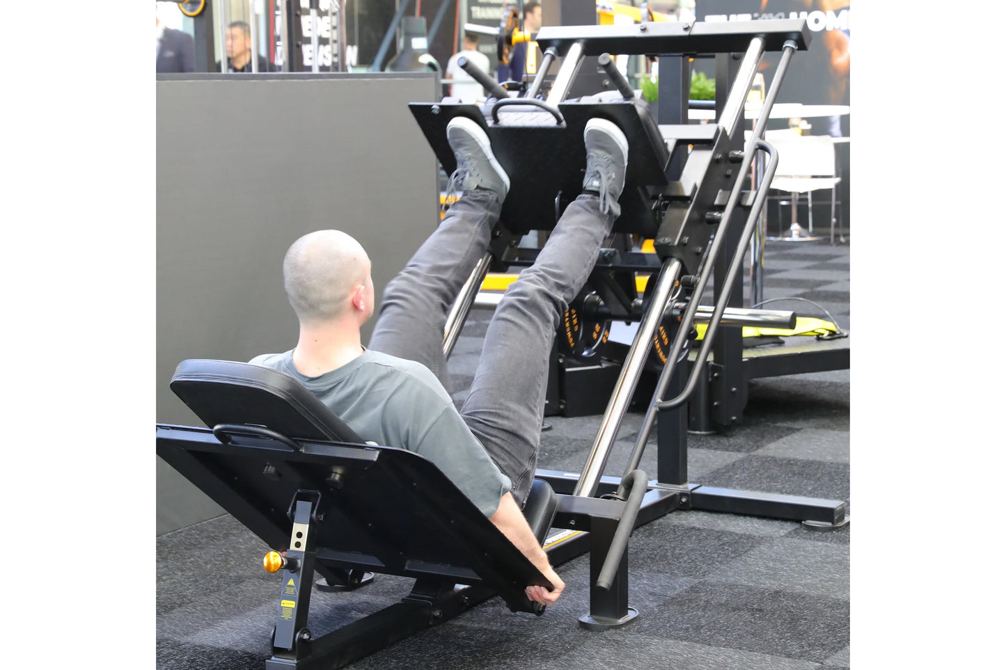Person using black and silver leg press hack squat combo machine in gym setting, demonstrating exercise form