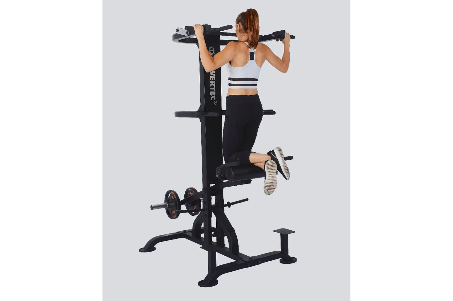 Black multi-station home gym with chin-up and dip bars, worn by woman demonstrating leg raise exercise on white background