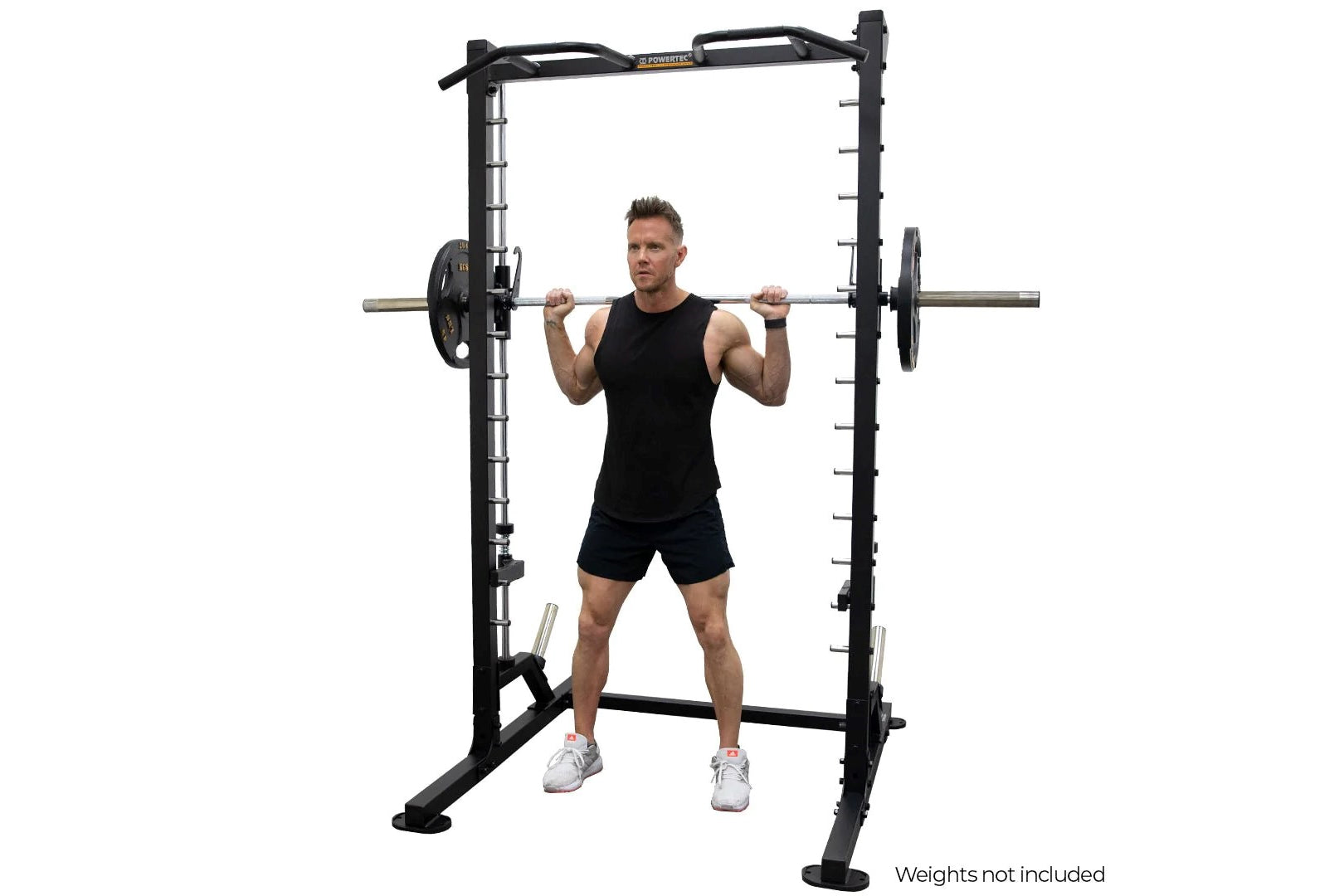 Black power rack with linear bearing smith machine system, man in black tank top and shorts performing barbell squat, white b