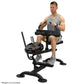 Male model using black seated calf raise machine with weight plate storage, demonstrating exercise form on white background