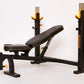Black and yellow Olympic weight bench with dual squat racks and adjustable leg extension, on white background