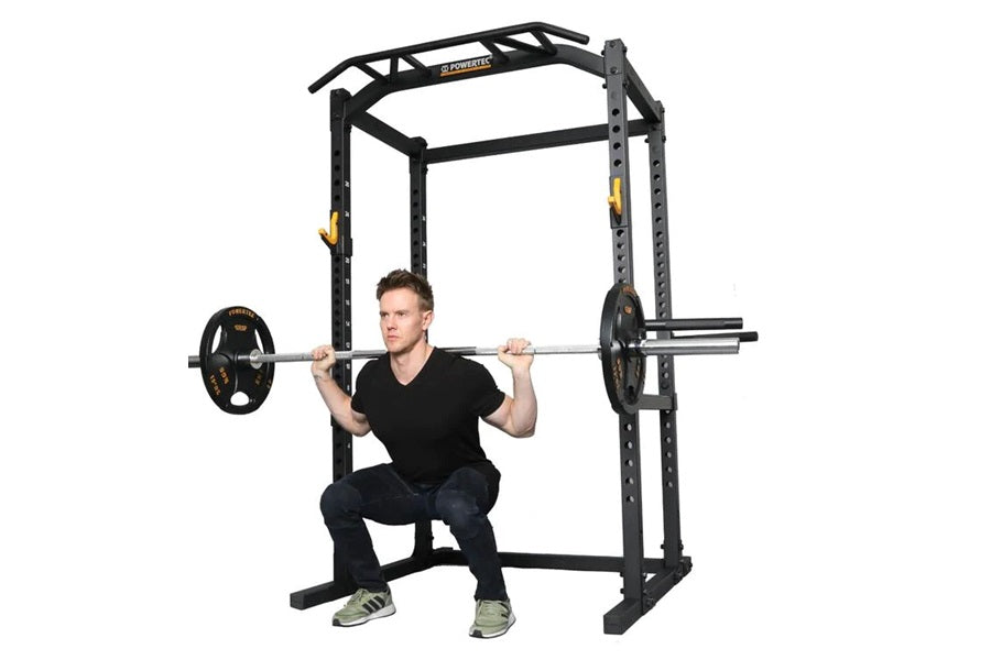 Black power rack with integrated pull-up bar and safety arms, shown with male model demonstrating squat position with loaded 