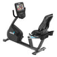 Black recumbent exercise bike with attached digital display console, pedals, and mesh backrest on white background