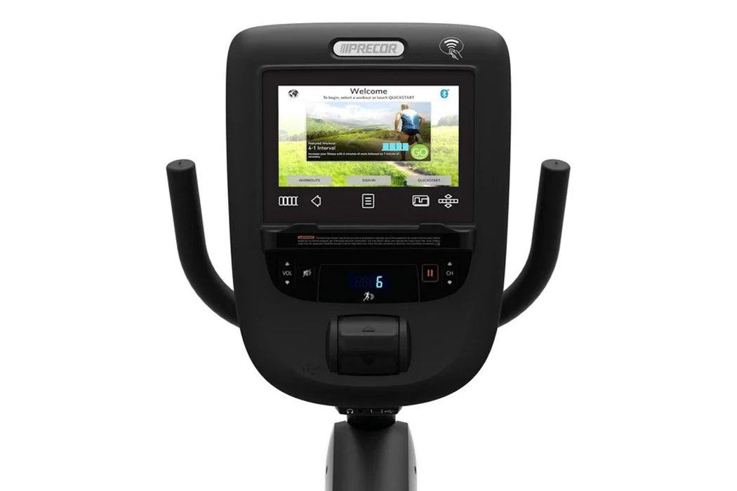 Precor RBK 865 recumbent exercise bike with black frame, curved handlebars, digital console displaying welcome screen, and co