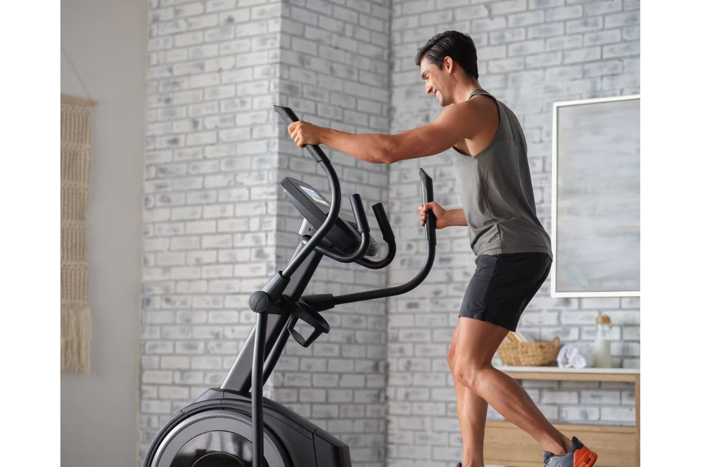 Man using black ProForm elliptical machine with digital console in modern loft-style bedroom with brick walls