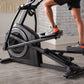 Person wearing gray sneakers with orange accents using black ProForm Carbon E7 elliptical machine indoors