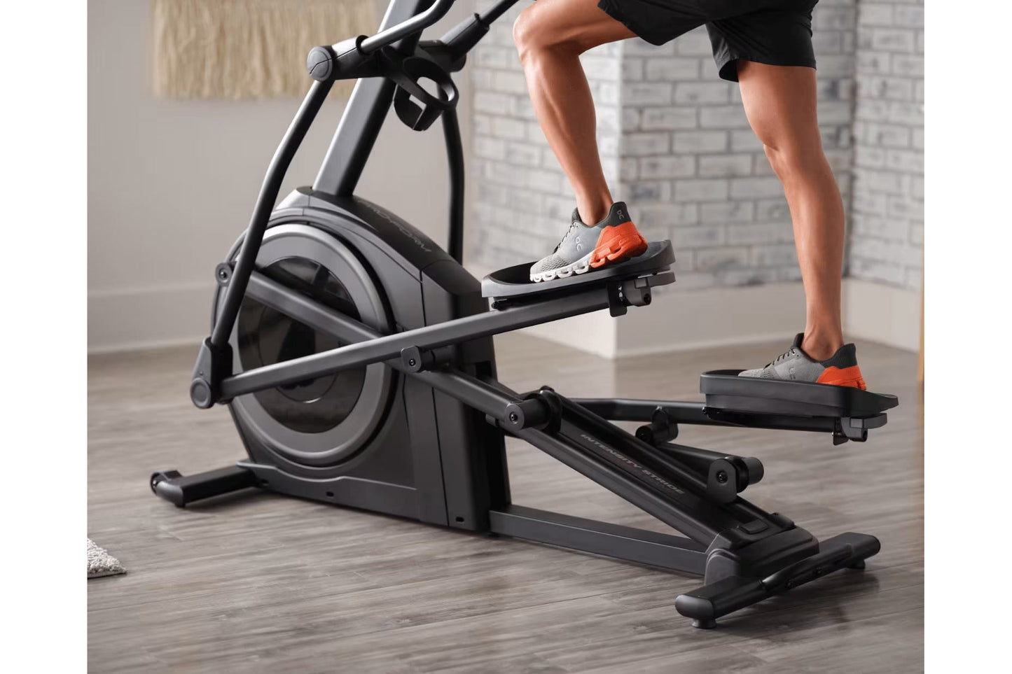 Person wearing gray sneakers with orange accents using black ProForm Carbon E7 elliptical machine indoors