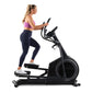 Woman wearing purple sports bra and navy leggings using black ProForm Carbon E7 elliptical machine on white background