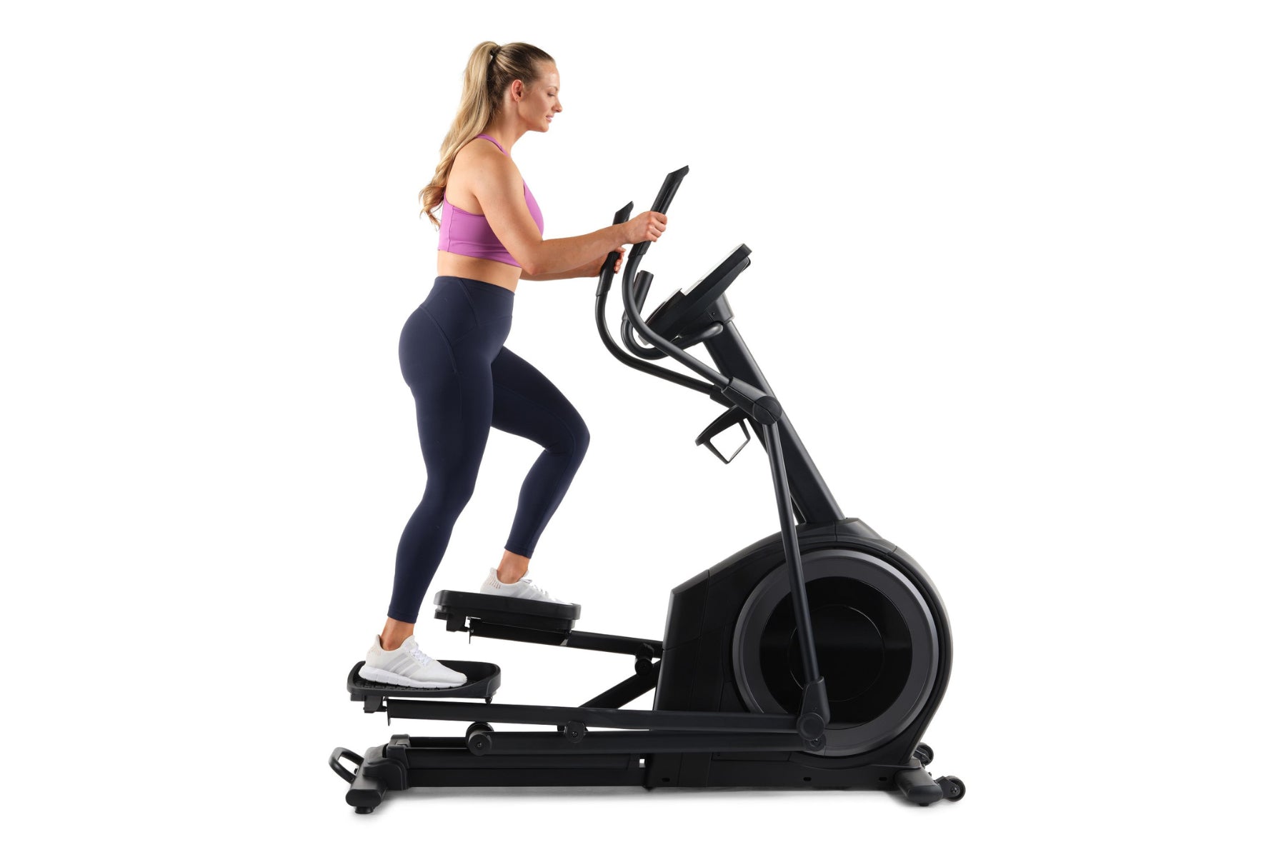 Woman wearing purple sports bra and navy leggings using black ProForm Carbon E7 elliptical machine on white background