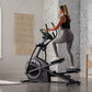 Woman using black ProForm Carbon E7 elliptical machine with digital display in modern home gym setting