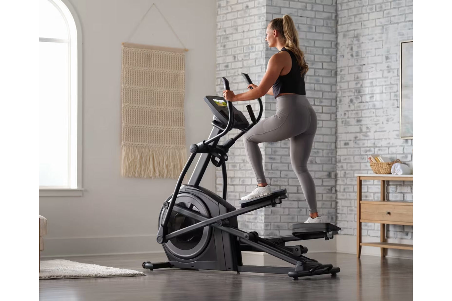 Woman using black ProForm Carbon E7 elliptical machine with digital display in modern home gym setting