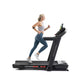 Woman running on black ProForm Carbon Pro 9000 treadmill with digital display, wearing gray sports bra and blue leggings