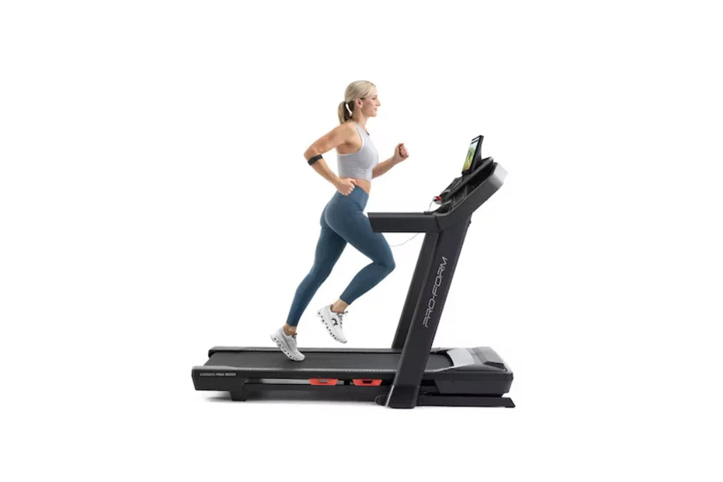 Woman running on black ProForm Carbon Pro 9000 treadmill with digital display, wearing gray sports bra and blue leggings