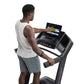 Man wearing white sleeveless shirt and gray shorts using black ProForm treadmill with digital touchscreen display