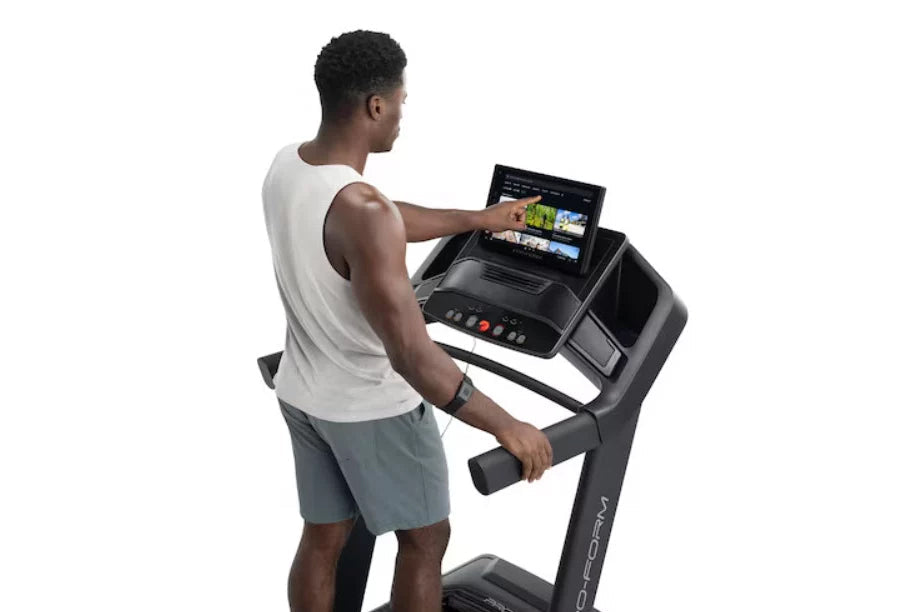 Man wearing white sleeveless shirt and gray shorts using black ProForm treadmill with digital touchscreen display