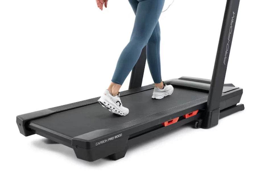 Woman running on black ProForm Carbon Pro 9000 treadmill wearing blue leggings and white sneakers