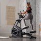 Woman using black ProForm Plus Carbon E7 elliptical machine with digital display in home gym setting