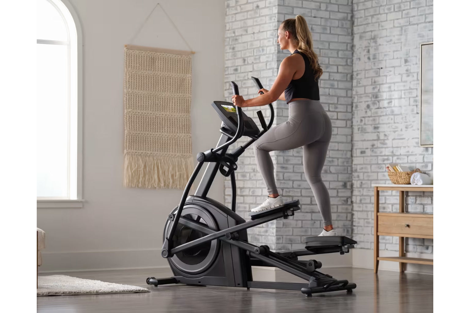 Woman using black ProForm Plus Carbon E7 elliptical machine with digital display in home gym setting
