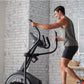 Man using black Proform Plus Carbon E7 elliptical with digital display in home gym with white brick walls