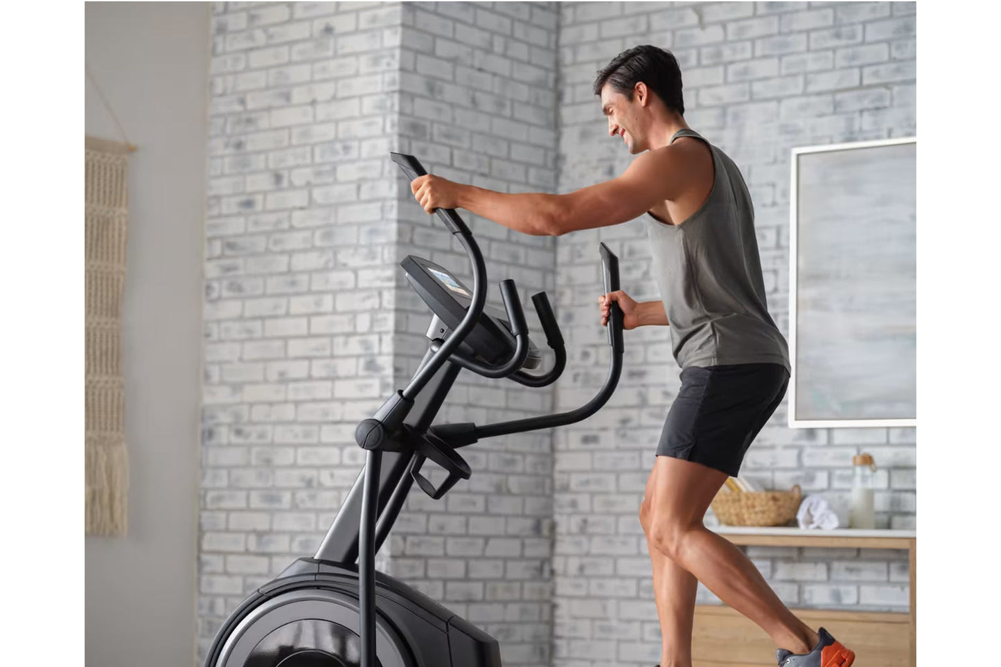 Man using black Proform Plus Carbon E7 elliptical with digital display in home gym with white brick walls