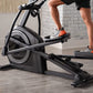 Person in black shorts and gray and orange sneakers using black and gray stationary exercise bike in home gym setting