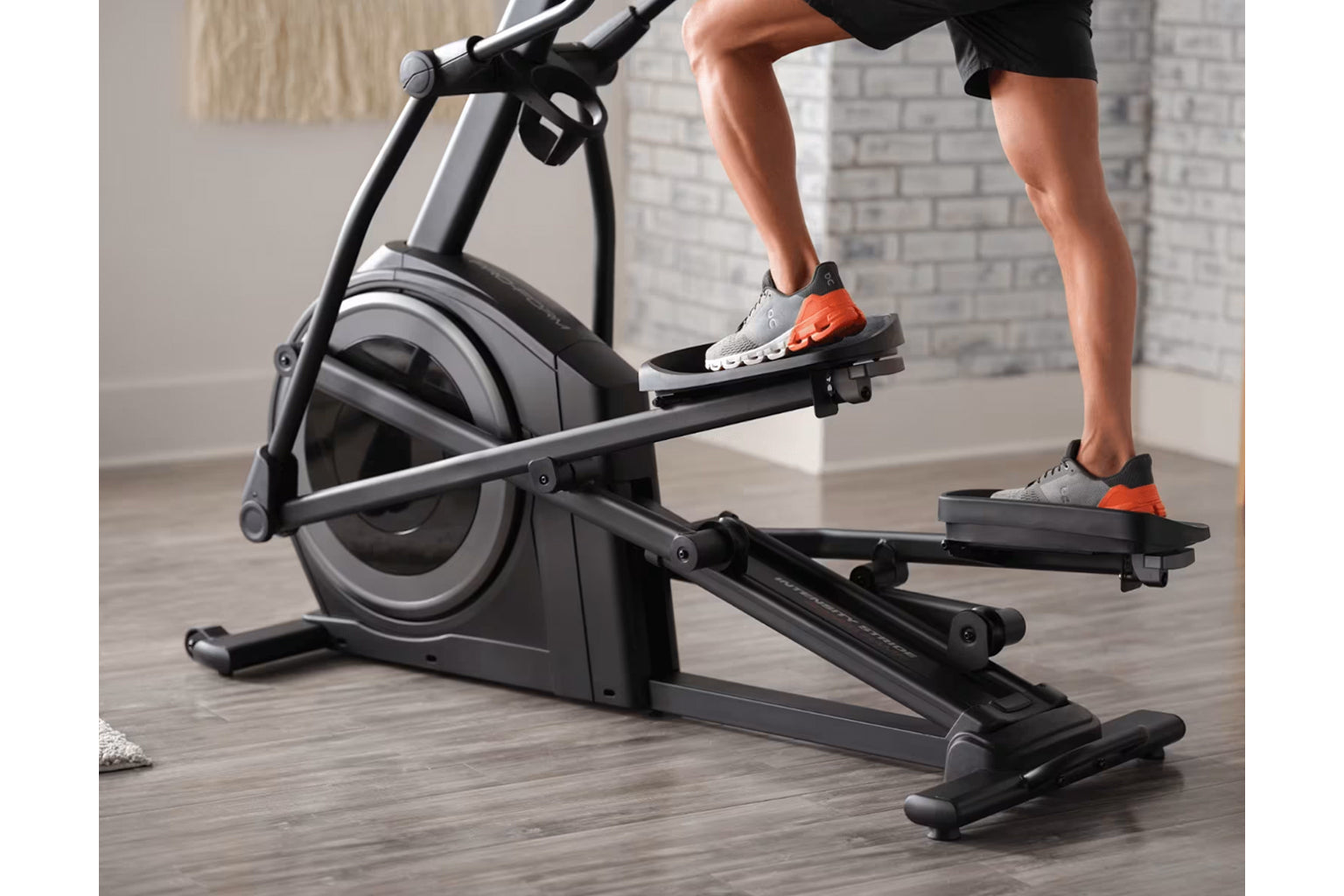 Person in black shorts and gray and orange sneakers using black and gray stationary exercise bike in home gym setting