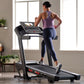 Woman wearing purple racerback tank and navy leggings running on black motorized treadmill with digital display in bright hom