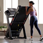 Woman running on black ProForm Plus Trainer 1000 treadmill with digital display in modern home gym setting