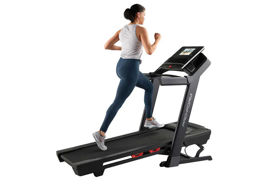 Woman running on black Proform Plus Trainer 1000 treadmill with digital display, wearing gray tank top and navy leggings