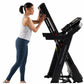 Woman using black Proform Plus Trainer 1000 treadmill with digital display, wearing white tank top and navy leggings