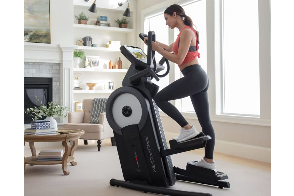 Woman wearing pink sports top and black leggings using black and white ProForm elliptical machine in bright home gym with fir