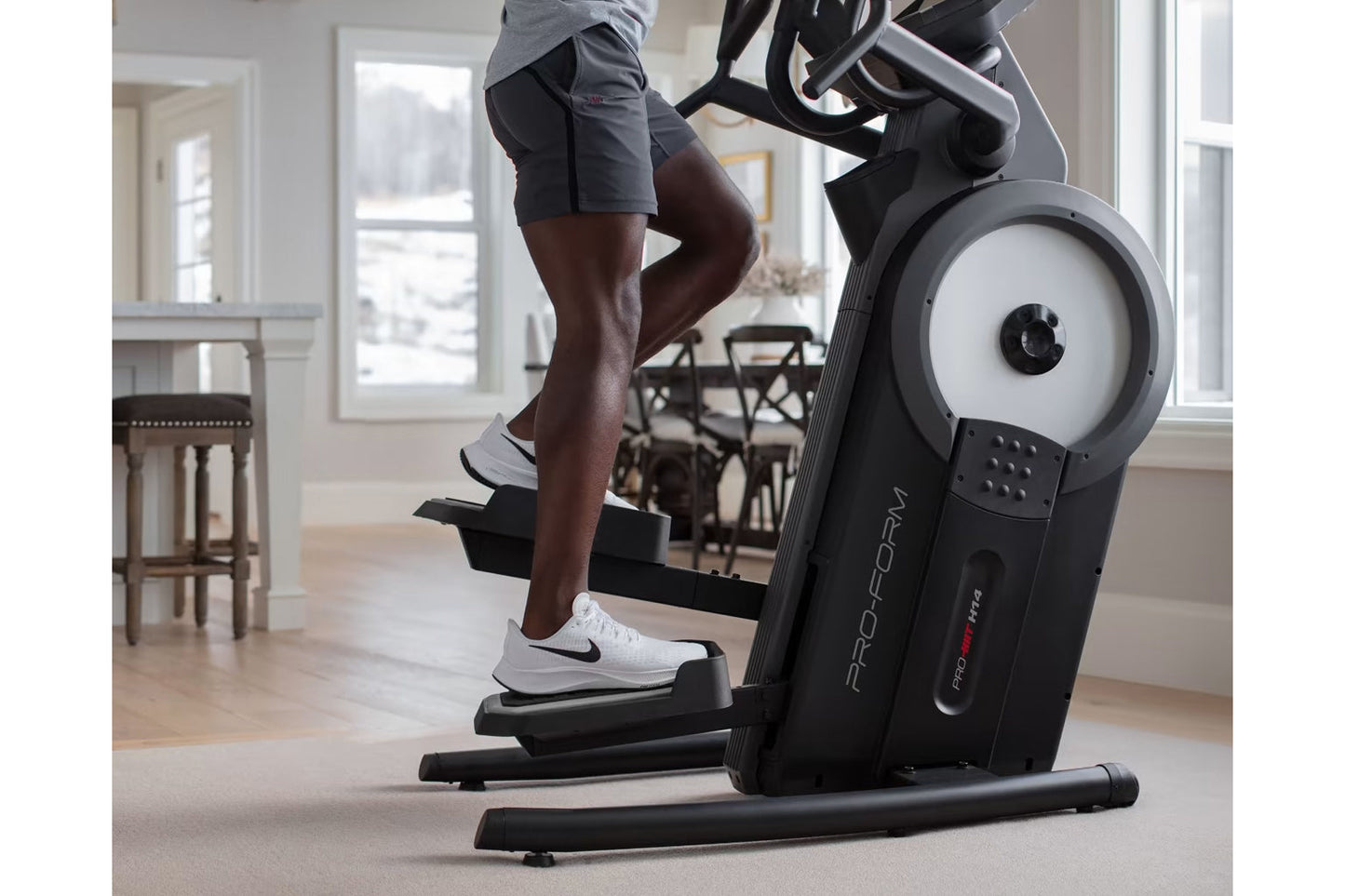 Person exercising on black ProForm elliptical machine with white wheel and handlebar in home gym setting