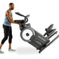 Man in blue tank top using black ProForm Pro HIIT H14 elliptical with white wheel and foot pedals on white background