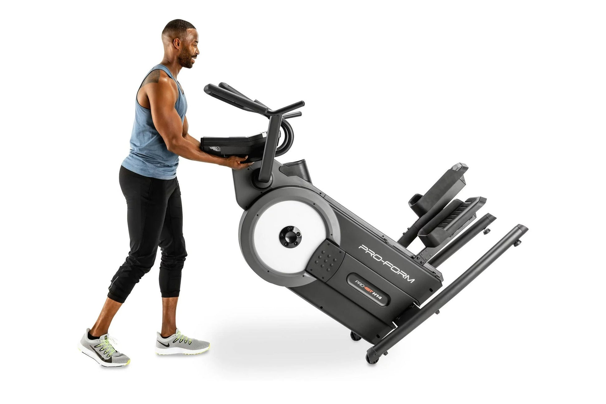 Man in blue tank top using black ProForm Pro HIIT H14 elliptical with white wheel and foot pedals on white background